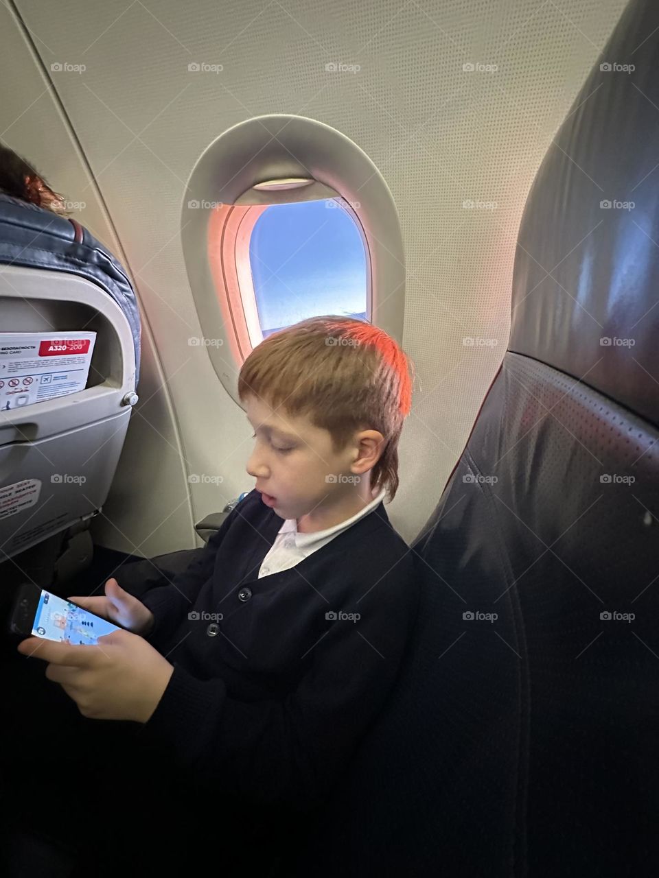 red-haired boy watching a movie on a smartphone in an airplane