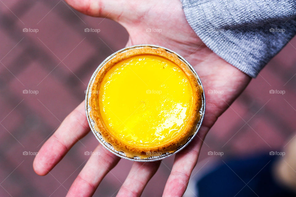 Hands holding a yellow egg custard tart
