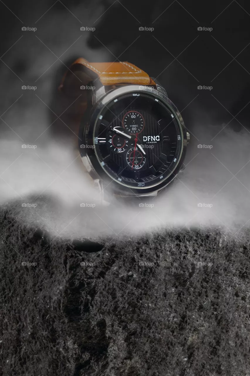 Brown leather strap wrist watch sat on stone with fog 