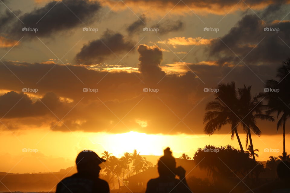 Silhouettes of man and woman, palms and clouds on a beautiful beach on sunset 