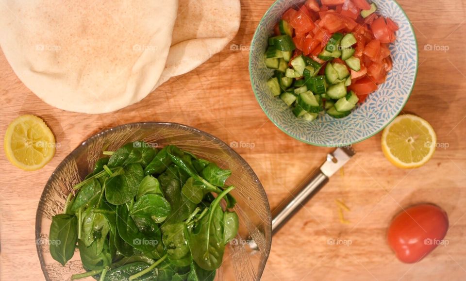 Fresh spinach salad cooking food prep with lemon, lemon zest, tomato, cucumber, and pita flat breads 