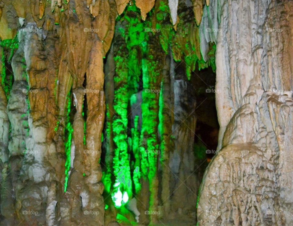 Long green glowing stalagmite formations mixed with natural walls of a limestone cave underground