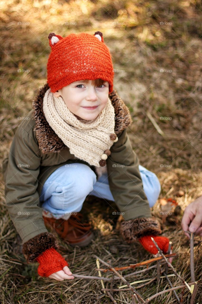 Little girl in a cap with fox ears with dad in the park builds a house of twigs