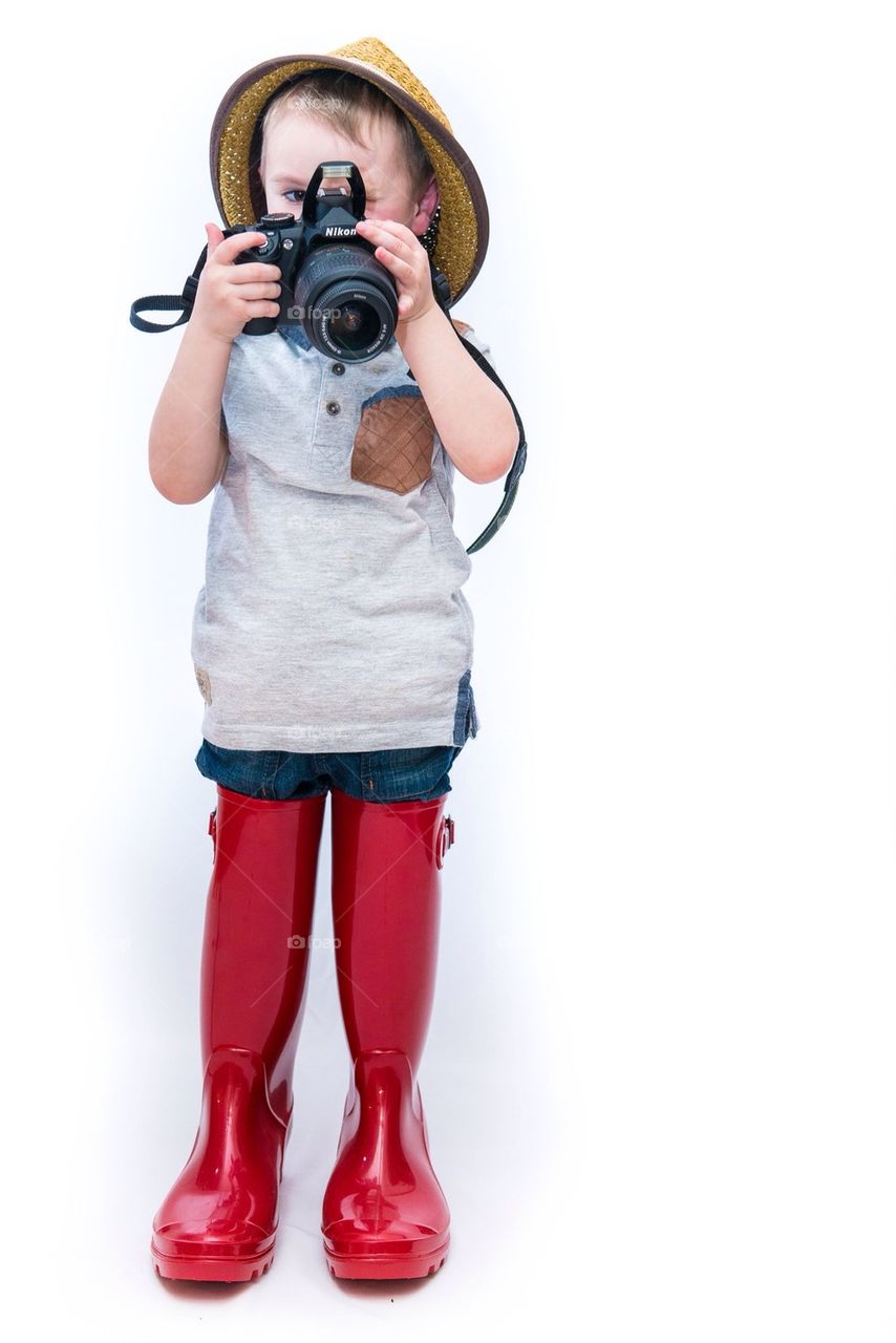 A young boy wearing oversized Wellington boots and holding a camera