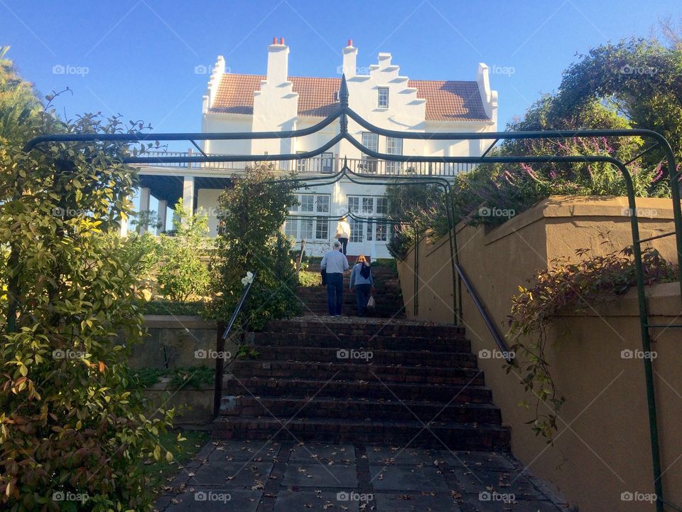 People walking up the stairs towards a beautiful old house on a sunny day in Winter at a boutique hotel in Cape Town 