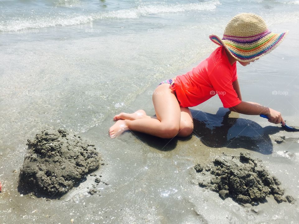 Little girl with fashionable summer hat playing in the sand on the beach