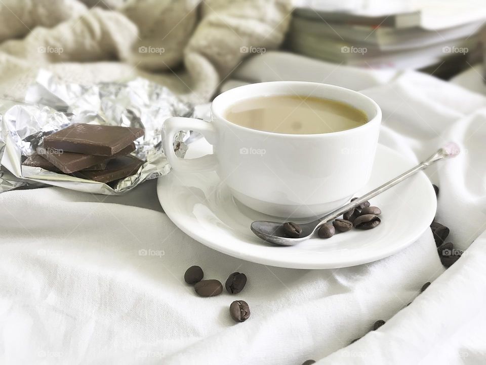 Coffee with chocolate in white bed with knitted sweater and magazines on background 