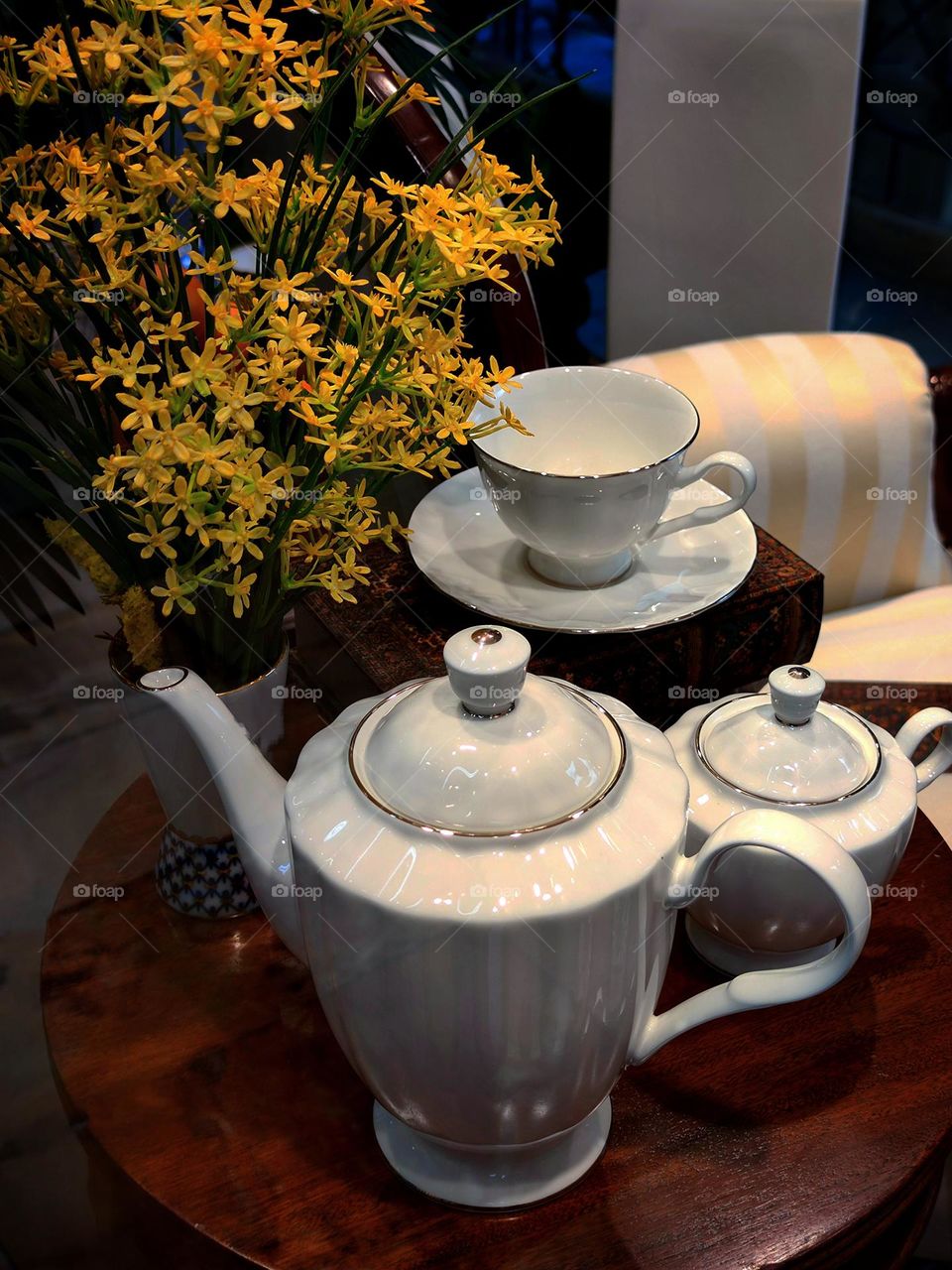 Wooden tea table with porcelain tea set and vase with yellow flowers
