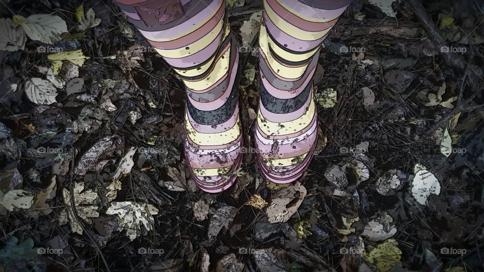 artistic picture of striped pink and yellow wellies standing in fallen dead autumn leaves and mulch in the woods