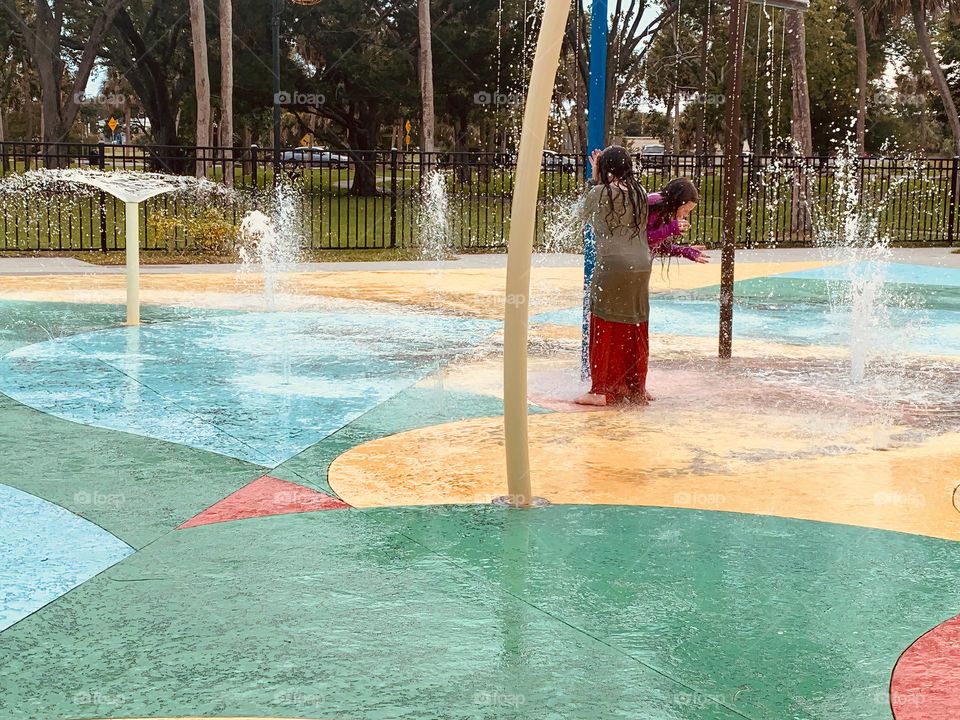 Children having lots of fun in the water at the colorful kids splash pad at the city park for children during a really warm day in Florida.