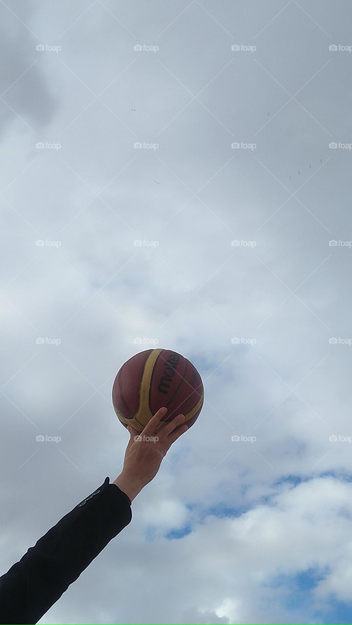 human hand holding a basketball high to hug the sky.