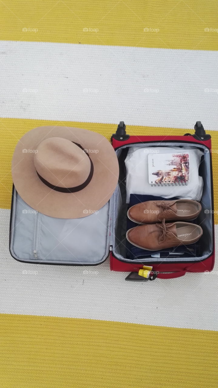 Packing simple way for a vacation. Big brown hat, Brown shoes white t-shirts and Prague book. Yellow colorful light.