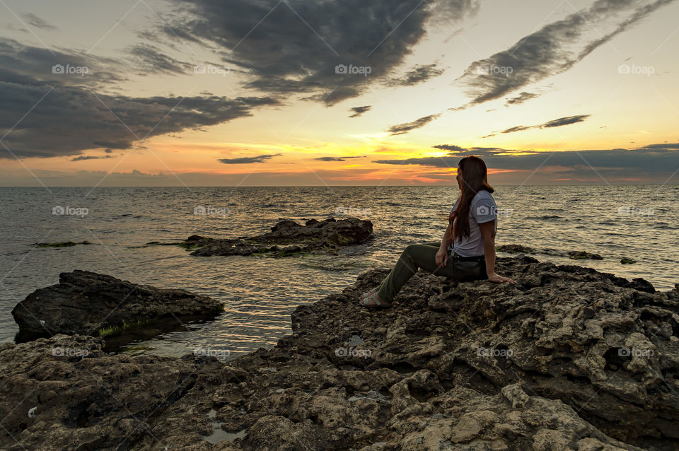 A young girl sits on the beach and looks at a beautiful evening, sea landscape, during sunset.