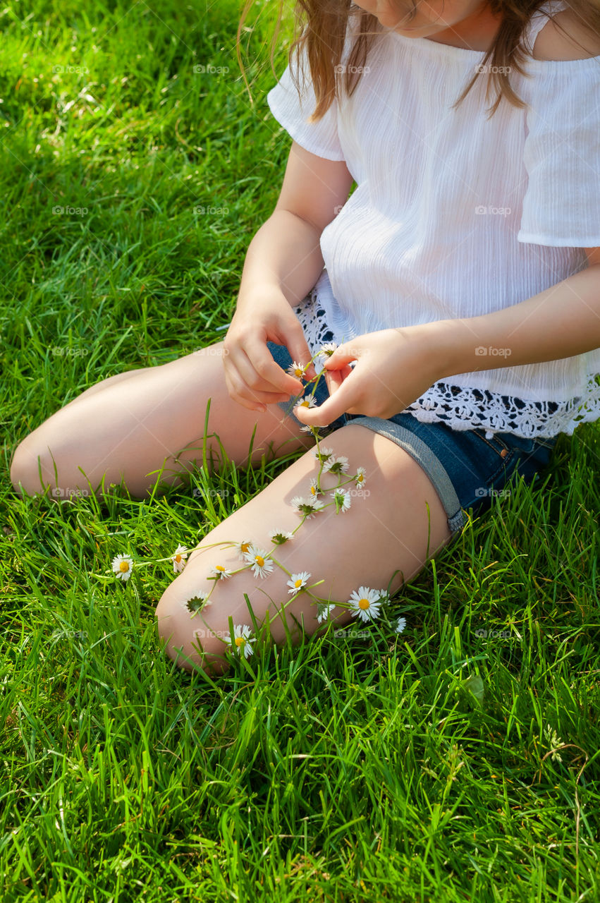 Girl with daisies flowers making a coronet. Daisy chain.