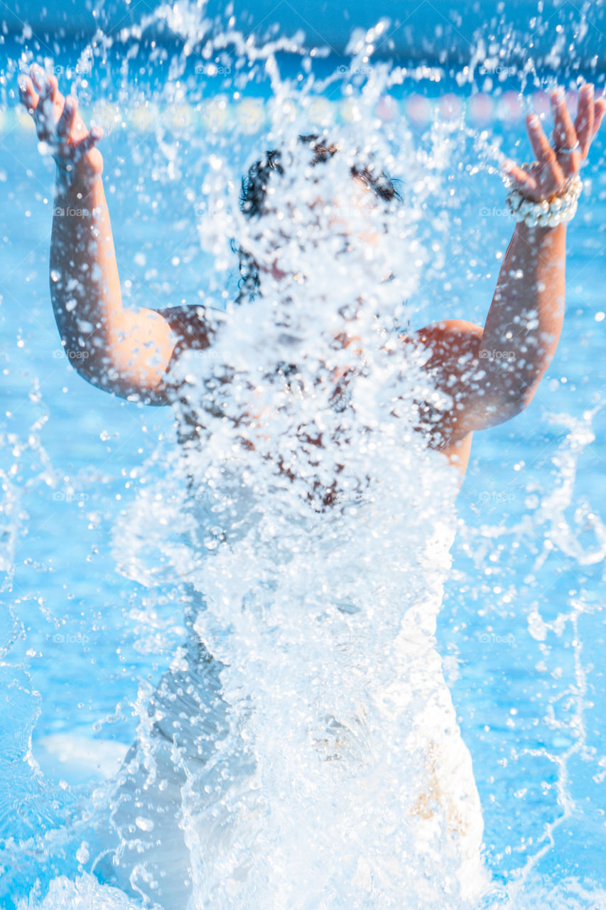 Bride wearing her bridal dress on her wedding day in the water in a swimming pool splashing water and having fun