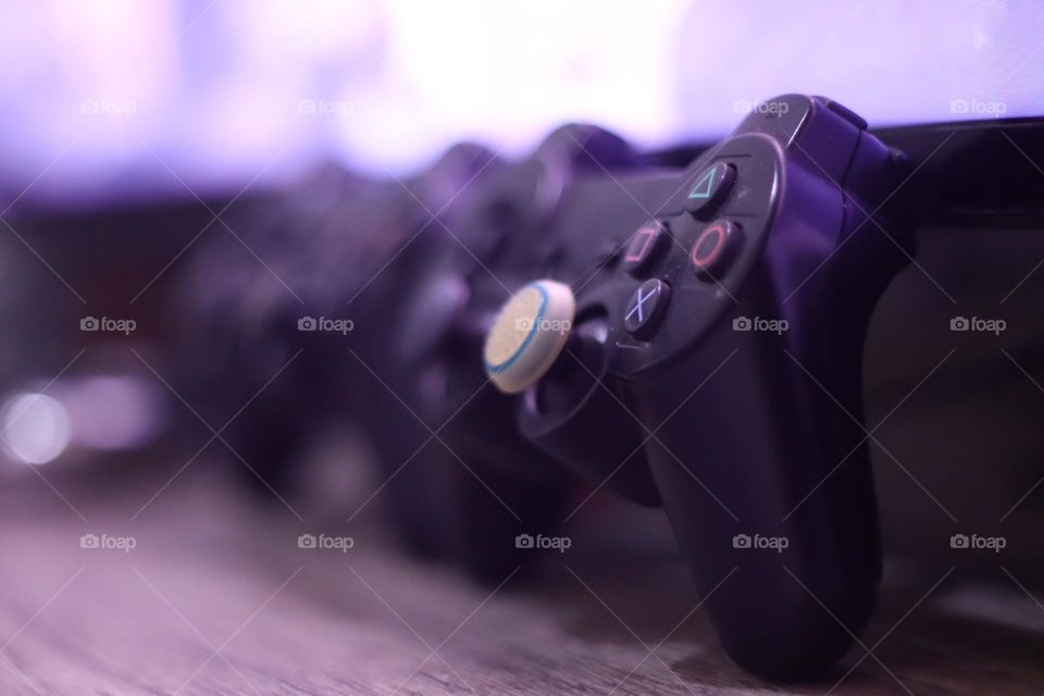 Two playstation gameapd sideways on the desk near TV blurry background.