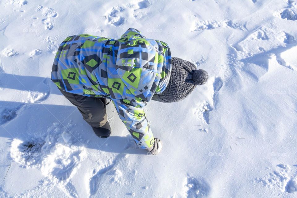 A child with a serious expression on his face in winter clothes jackets, pants, hat and boots in winter on the white snow on the street and in the park in nature plays winter fun.