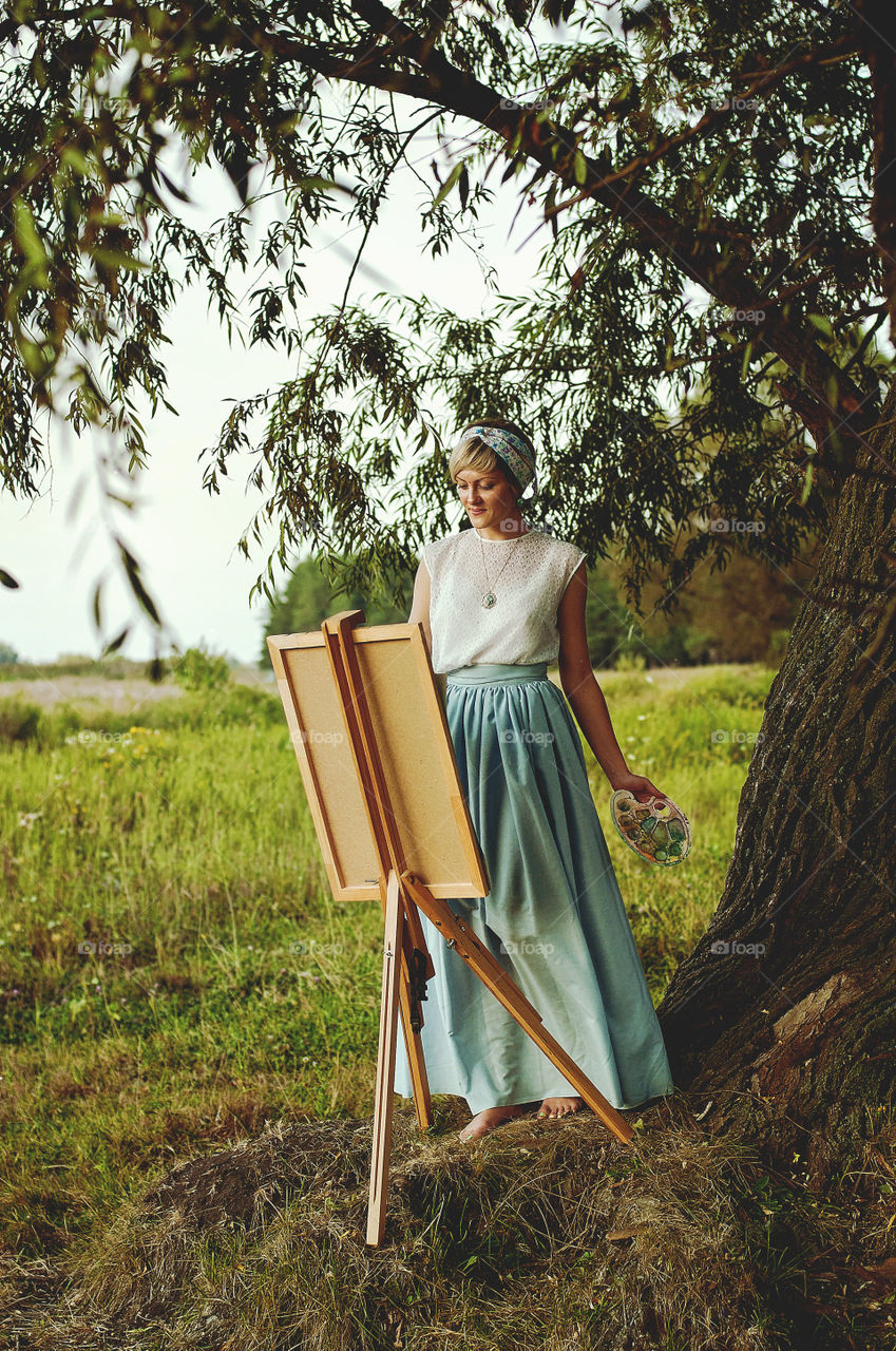 Lovely young woman artist paints her picture in autumn at sunset light in nature.