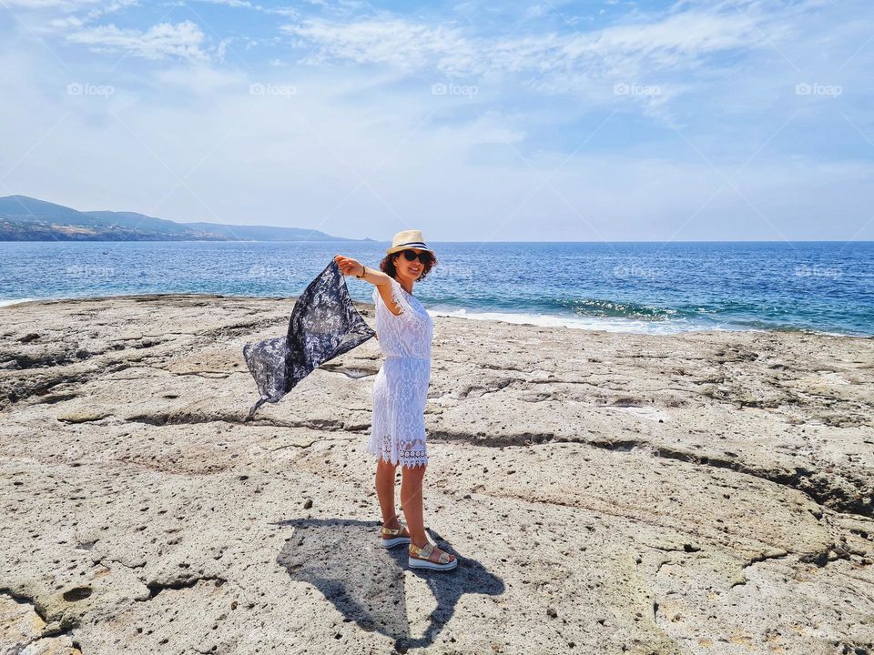 woman in white summer dress plays with the wind above the rocks