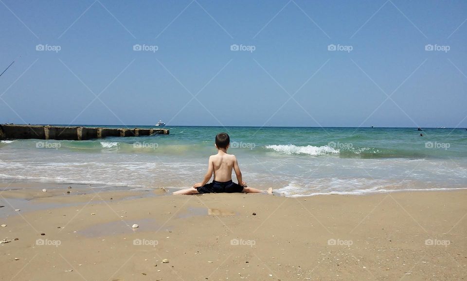 Kid sit in split position on the beach looking at the sea