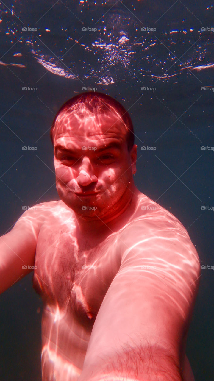 Man diving, man underwater smiling and relaxing in big blue sea