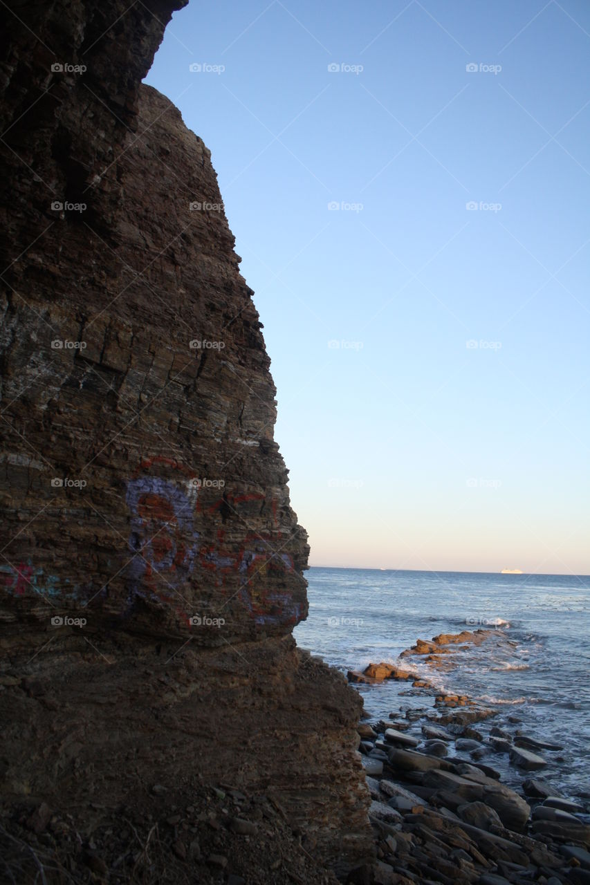 Rocky cliffs with faint graffiti painted on them near the sunken city of San Pedro. With a carnival cruise ship sailing in the far distance 
