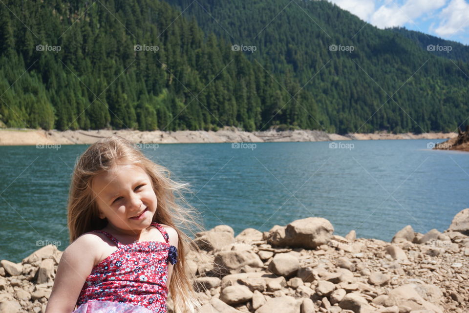Little girl with straight long blond hair in a red floral swimsuit at the lake on a sunny day