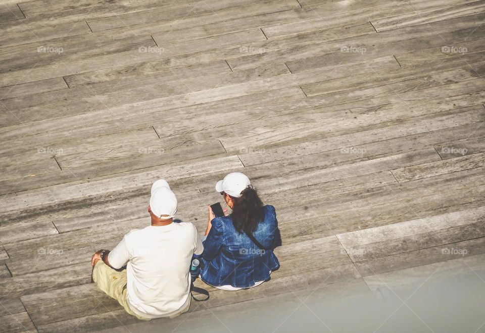 A woman looking on her phone sitting on the boardwalk.