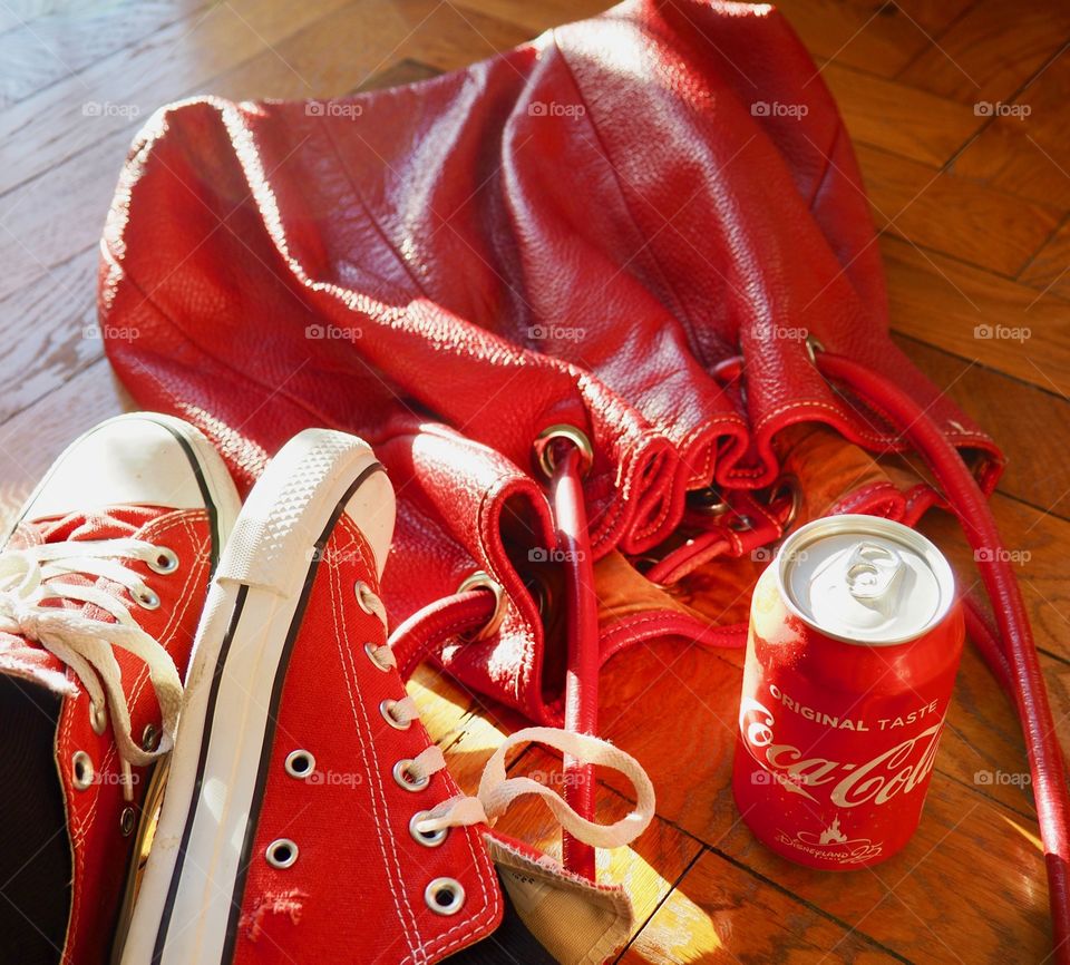 Can of Coca Cola on hardwood floor next to red bag and sneakers.