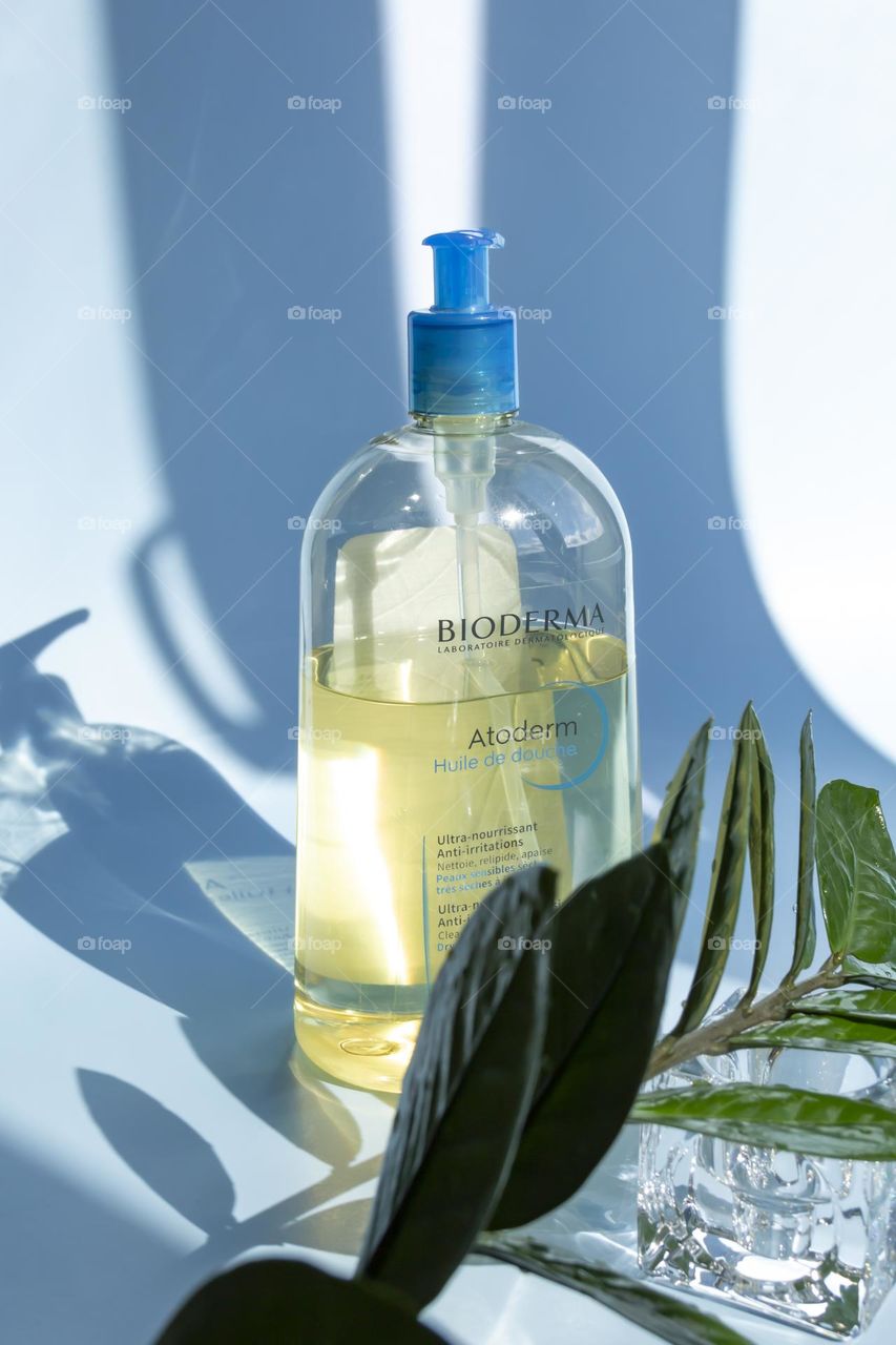 Cosmetic product Bioderma for skin care and showering on a blue background, with a green flower.