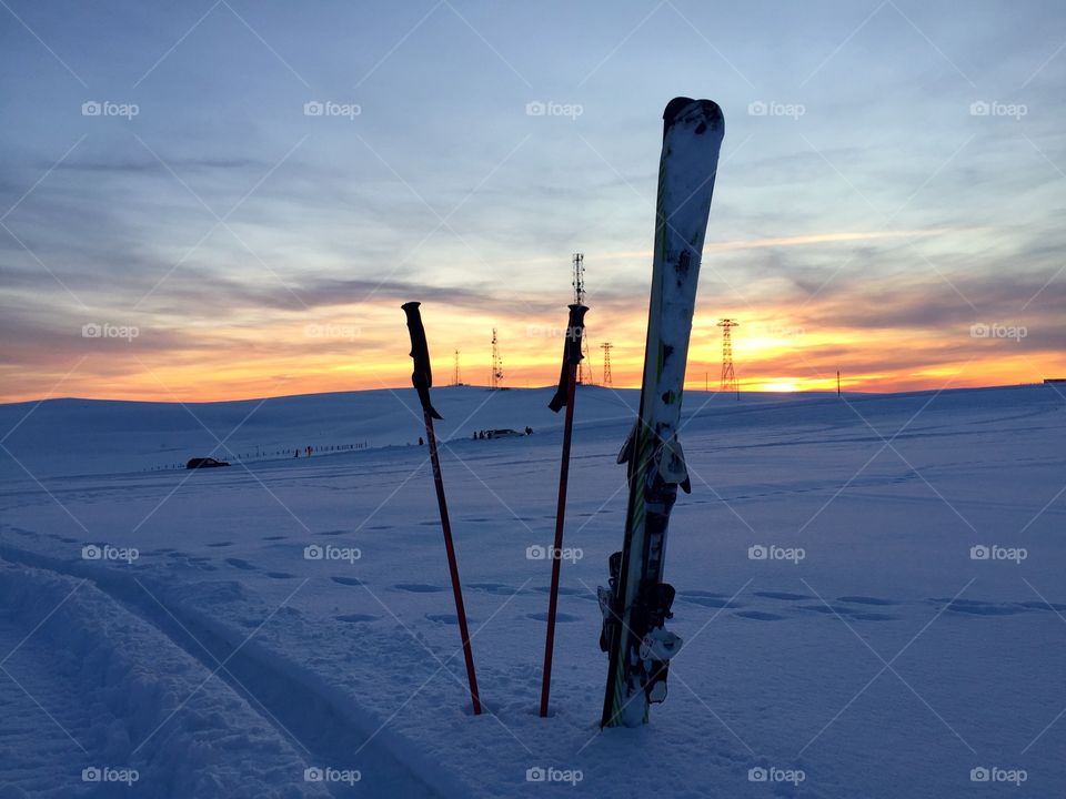 Skis and ski poles in the snow with sunset in the background 