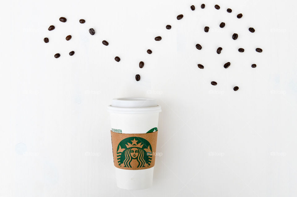 A Starbucks coffee cup laid out on a white table with coffee beans appearing to sprout out of the top