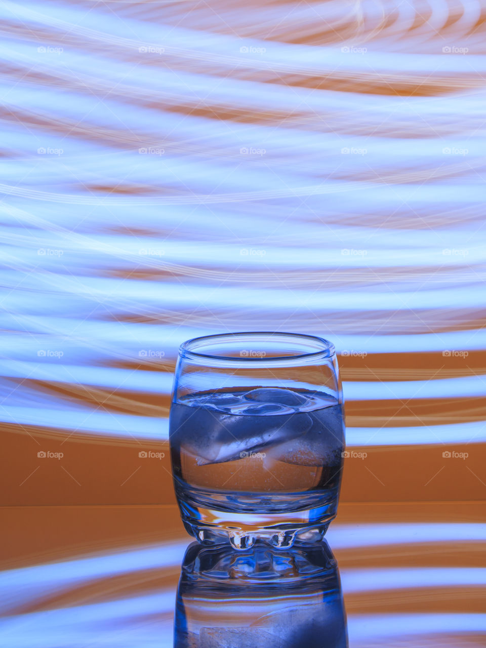 Misted up glass of cold water with blue ice on an orange background