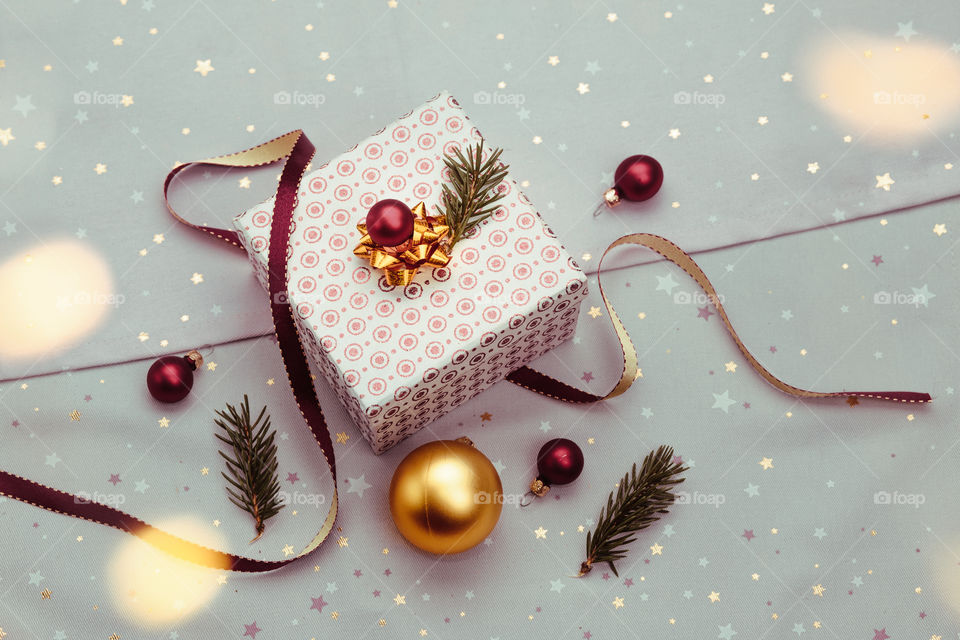 Wrapping Christmas gift into box. Decorating using red ribbon, red Christmas balls and pine twigs. Blurred Christmas lights. Flat top-down composition. Figure of angel made of earthen with love inscription as Christmas decoration