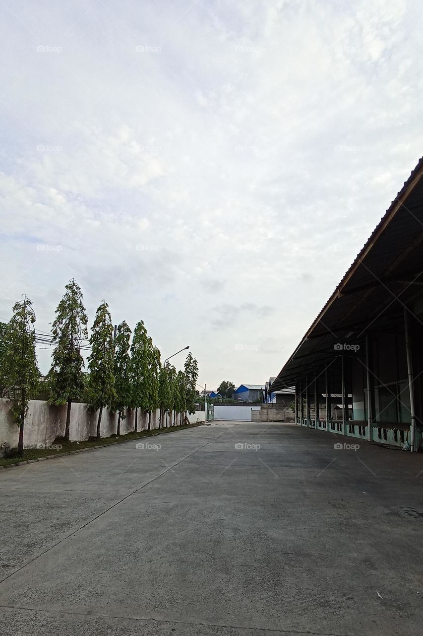 open area with a wide concrete floor, surrounded by buildings with long roofs and high white fences