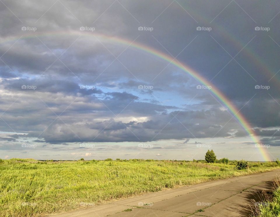 In the cloudy sky over a summer meadow, two bright rainbows