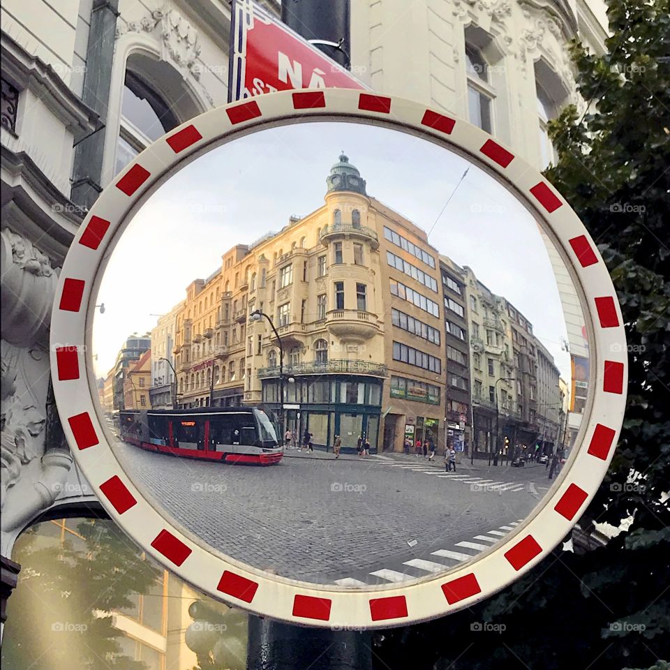 Round mirror in the street reflects old buildings and a tram