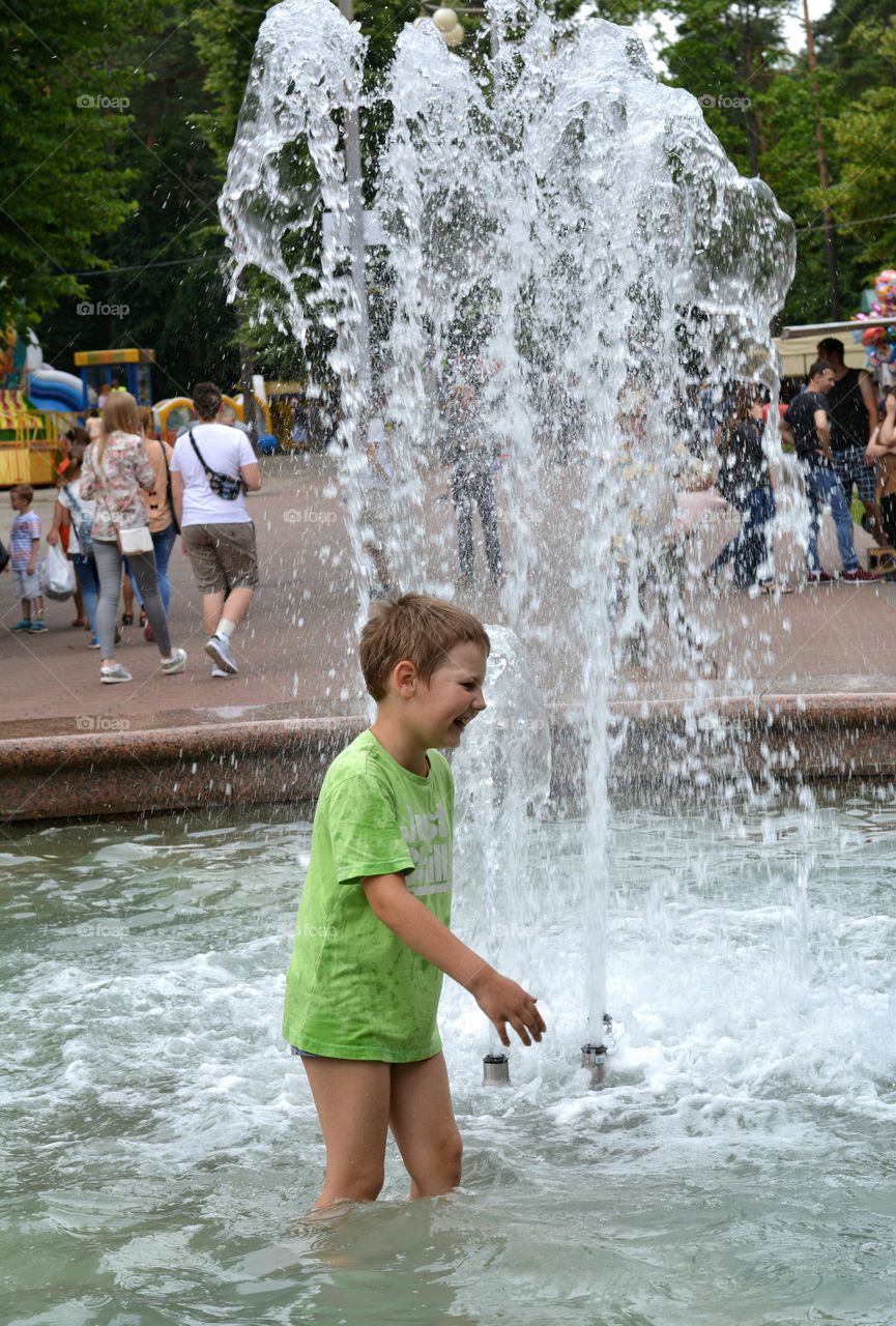 child boy in the water splash fountain, summer heat, city street view