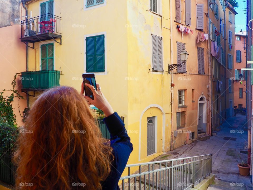 Redhead young woman taking photo with phone in the old town of Nice, France.