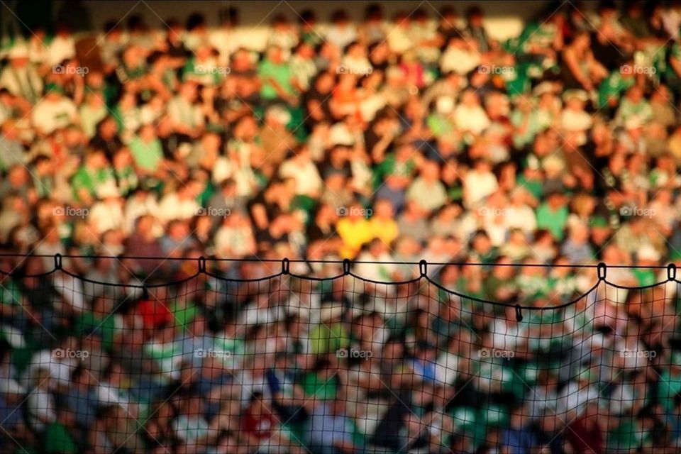 Crowds of people in a stadium on a grandstand in the evening sun