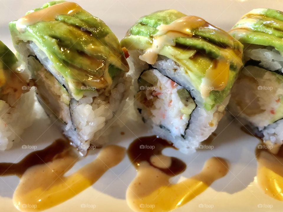 Fresh sushi topped with avocado sitting on top of a white dish
