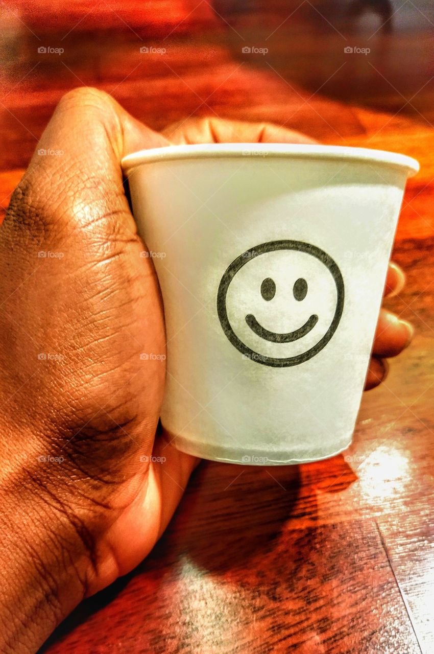 Hand holding a cup with a smiley face drawn on it