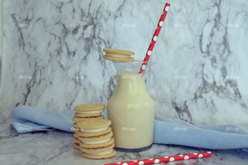 Oreo double stuff cookies stack next to a carafe of milk with a red and white straw on a marble backdrop