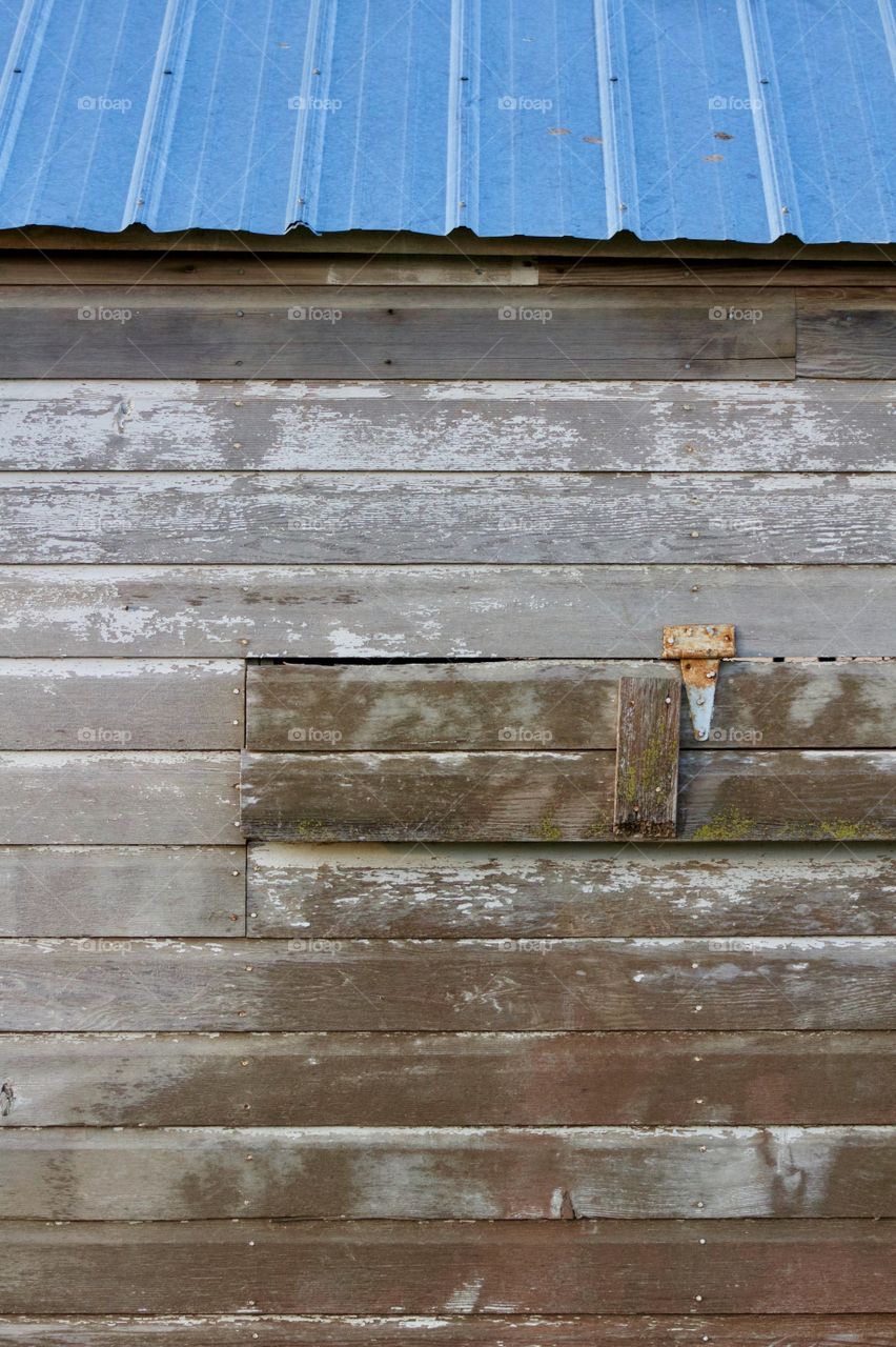 Rusted hinge on a weathered wooden ventilation opening in the siding of an antique farm building  