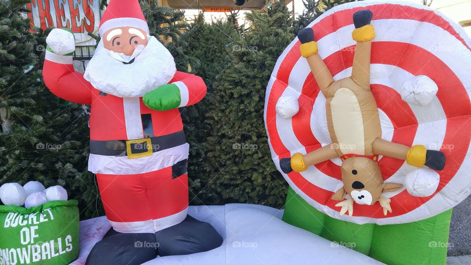 Inflated decoration of Santa Claus throwing snowballs at reindeer tied to a target.