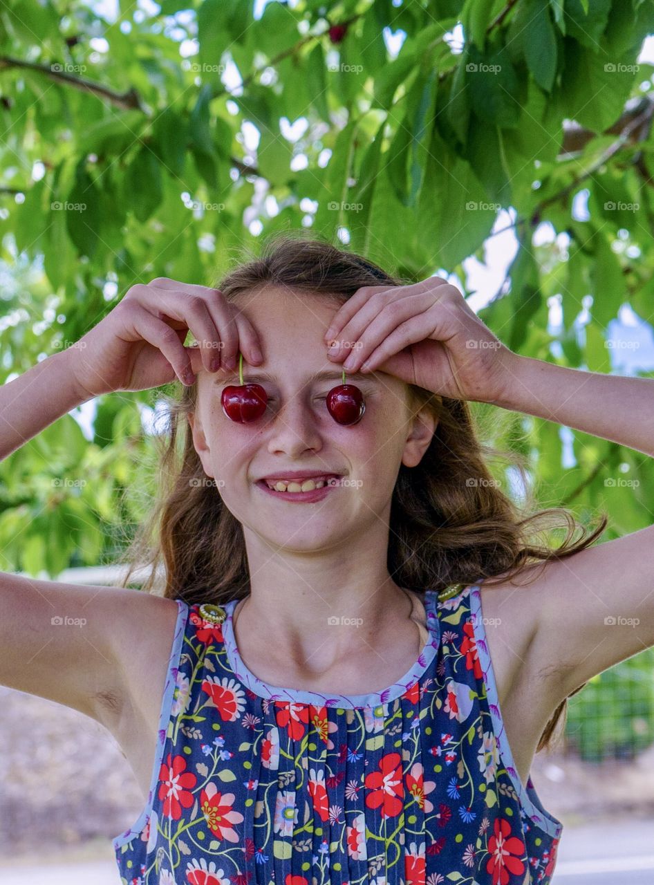 Girl makes funny cherry eyes under cherry tree