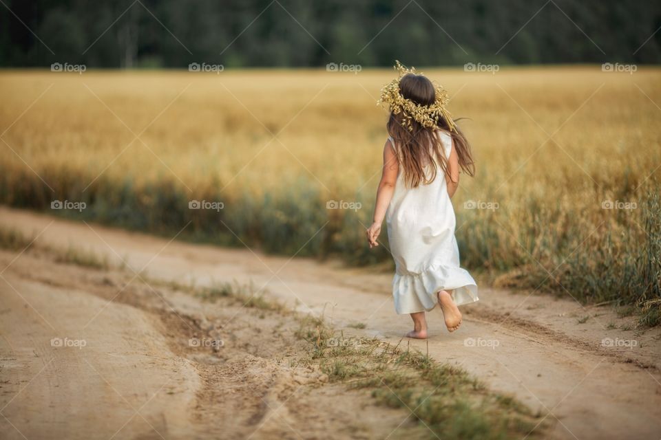Girl running on the sand road through the rye field 