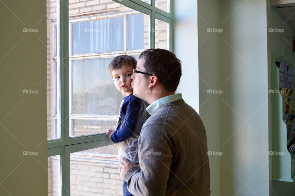 Father kissing son on the cheek while looking outdoors through a window