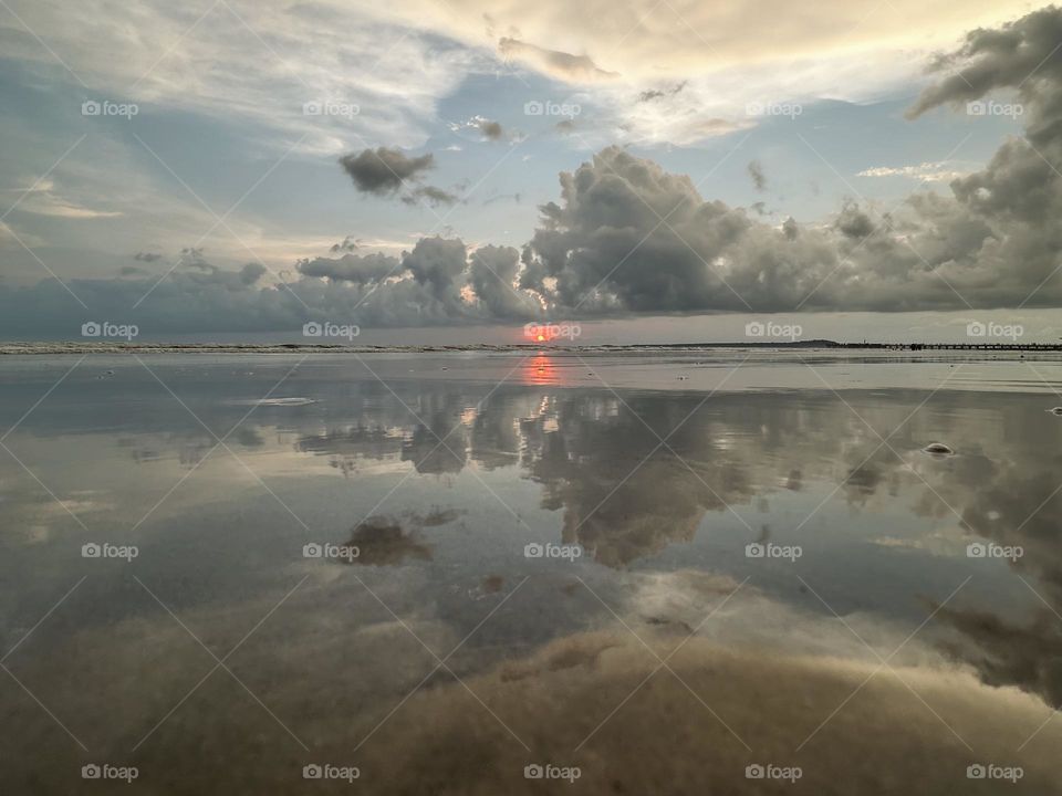 Amazing sunset reflected on the beachfront ocean, with the sky forming  beautiful clouds.