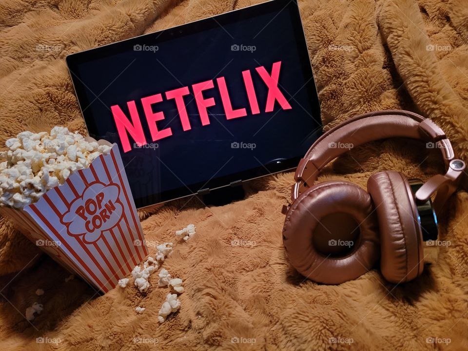 Laptop computer screen ready to watch Netflix for a fun, cozy, and relaxing night with popcorn as a snack, on soft bed blanket in room, with pink headphones